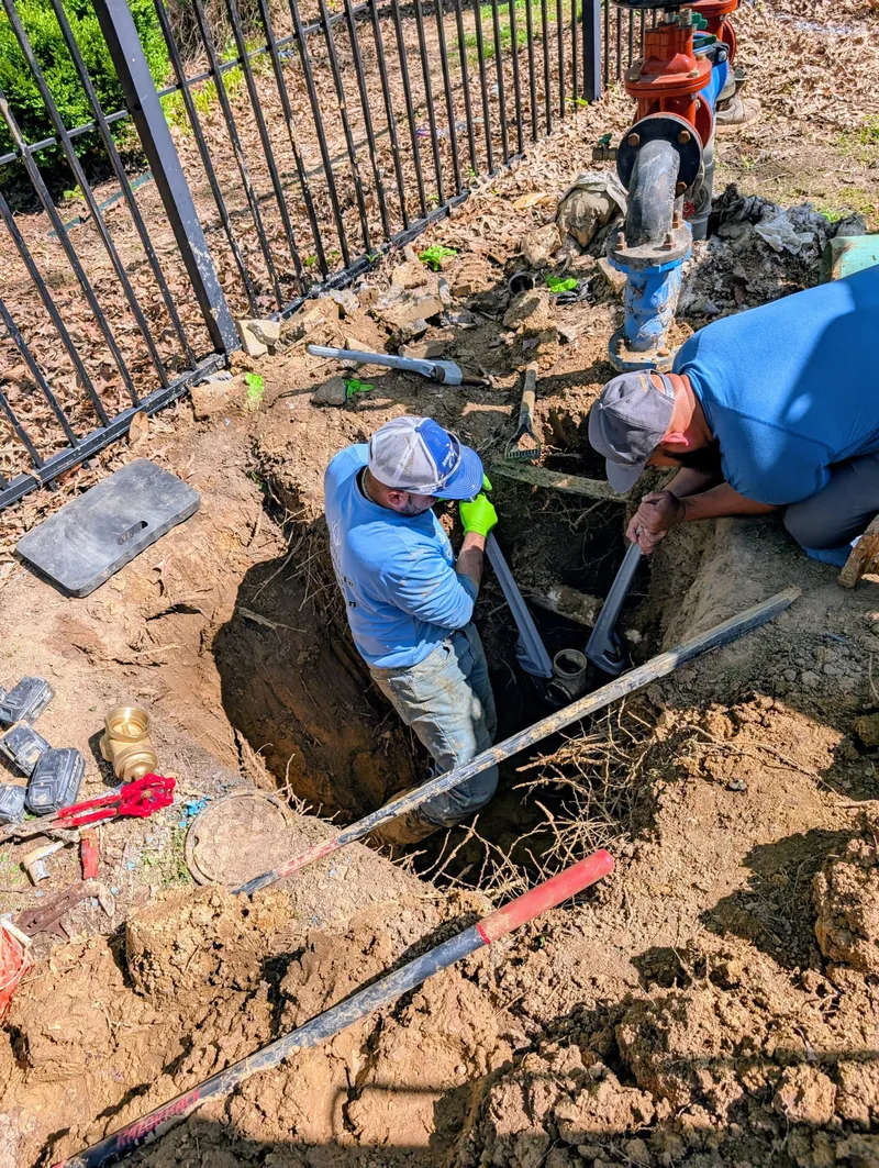 Two plumbers replacing and repairing a commercial RPZ backflow preventer in an excavated trench