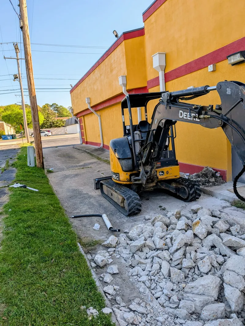 Mini excavator breaking up concrete outside a commercial building near UALR for sewer line replacement