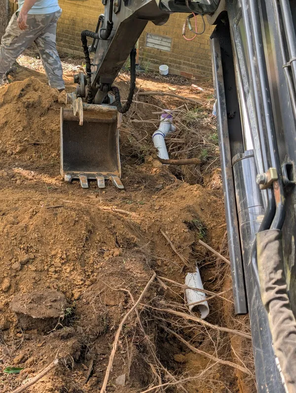 Mini excavator digging along a sewer line with new PVC fittings in the trench