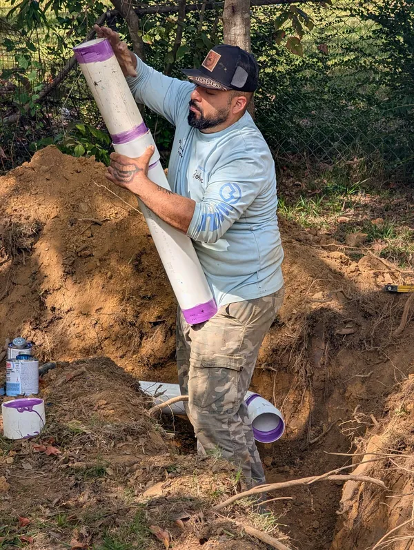 Diamond State Plumbing technician carrying a length of PVC sewer pipe to an open trench