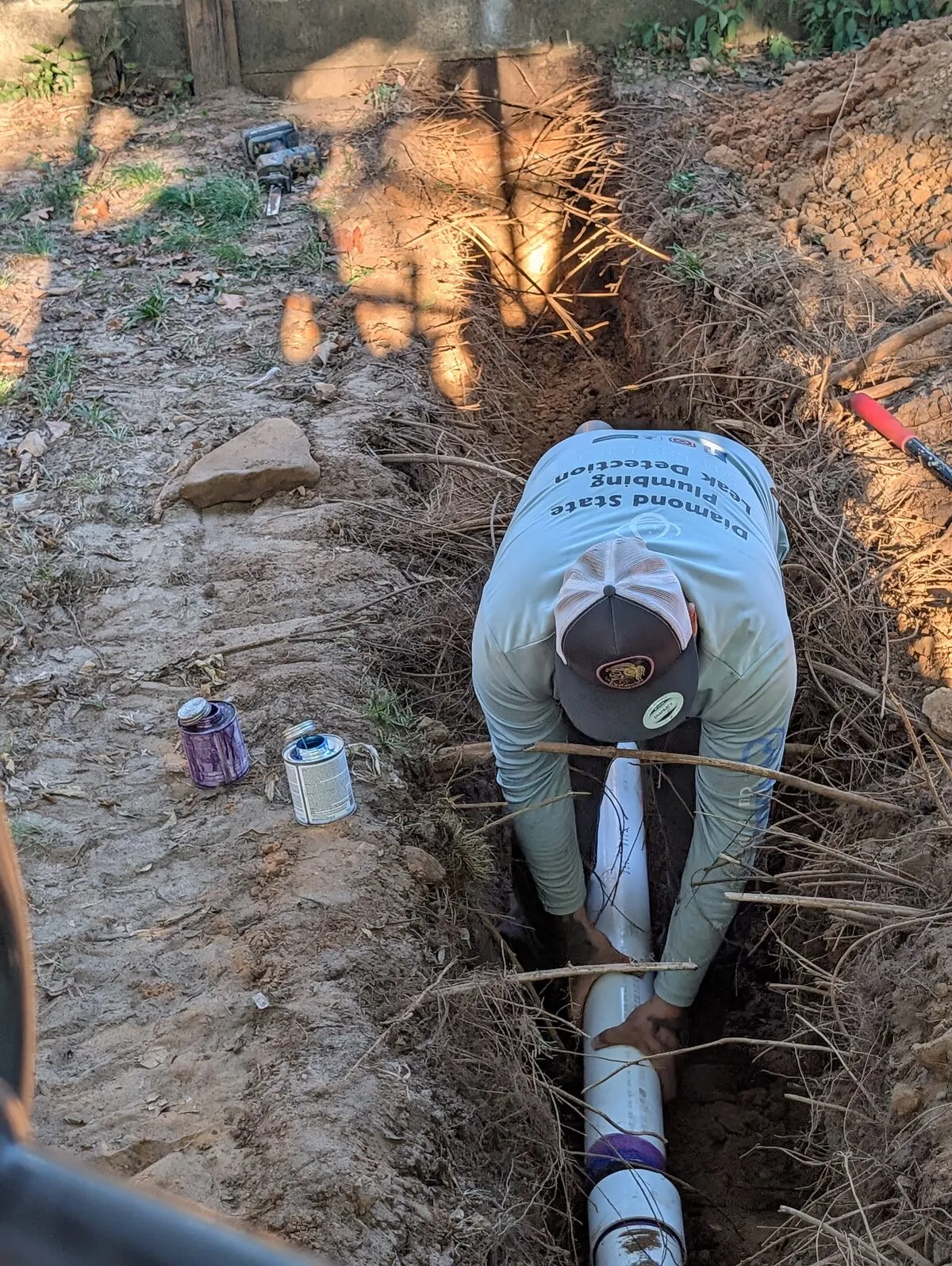 Technician fitting a new PVC sewer line through a trench full of tree roots