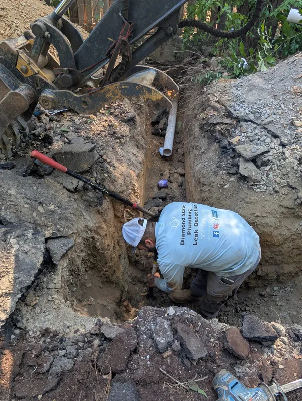 Diamond State Plumbing technician repairing a sewer line in a rocky trench