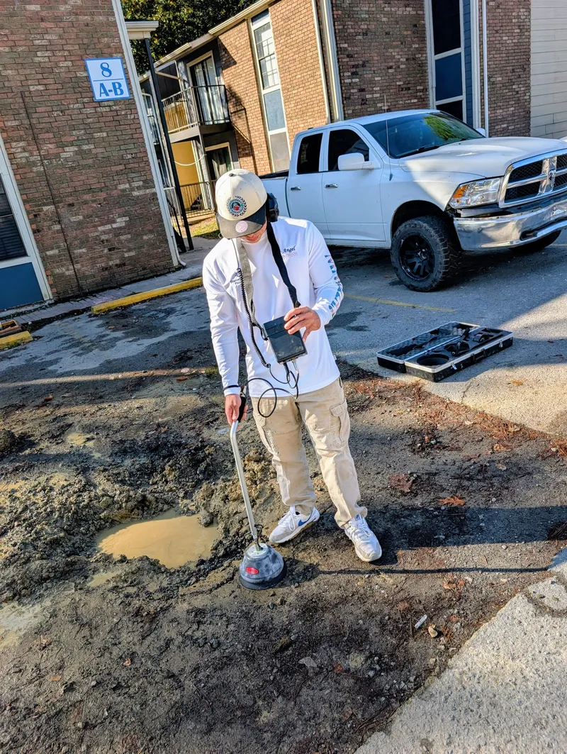 Plumber using electronic leak detection equipment in an apartment complex parking lot to locate an underground water leak